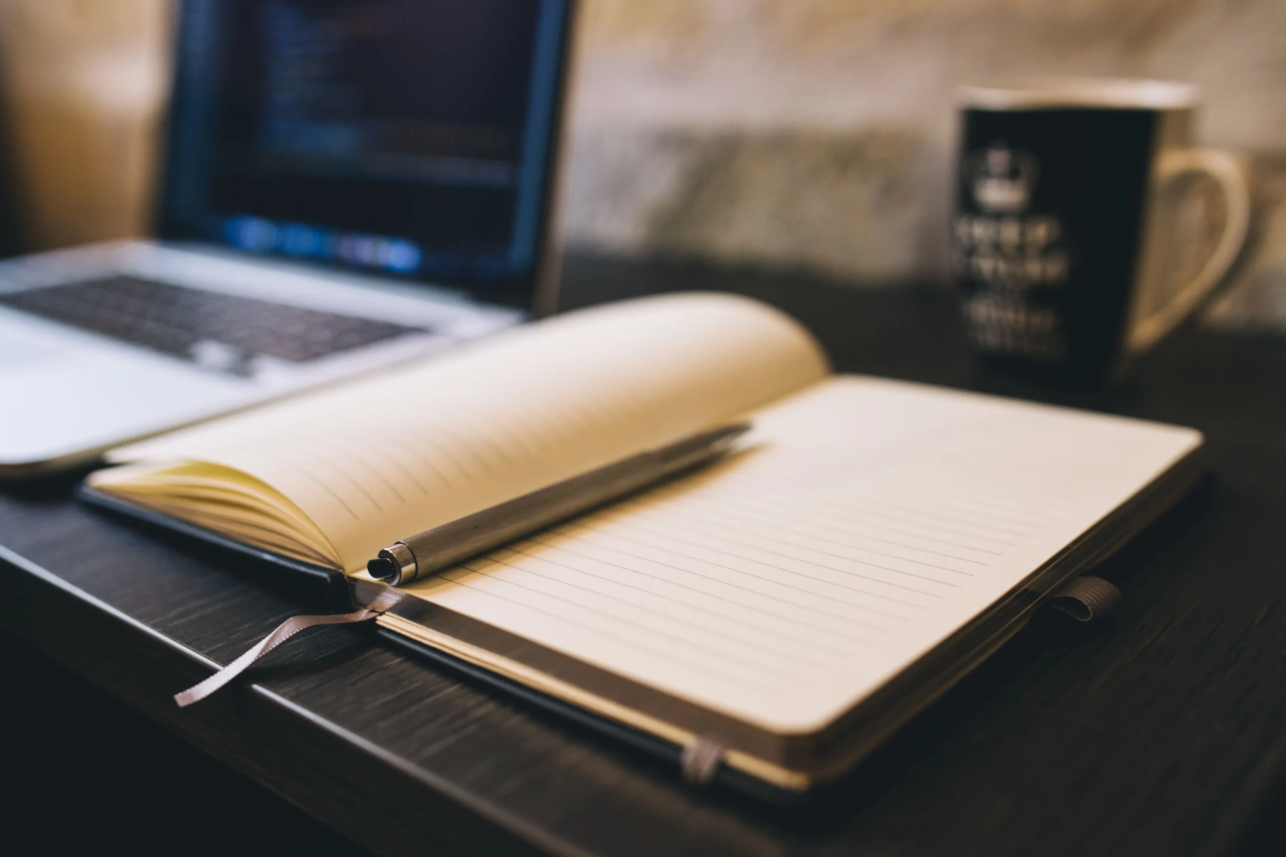 An open notebook on a black desk with a silver pen on it