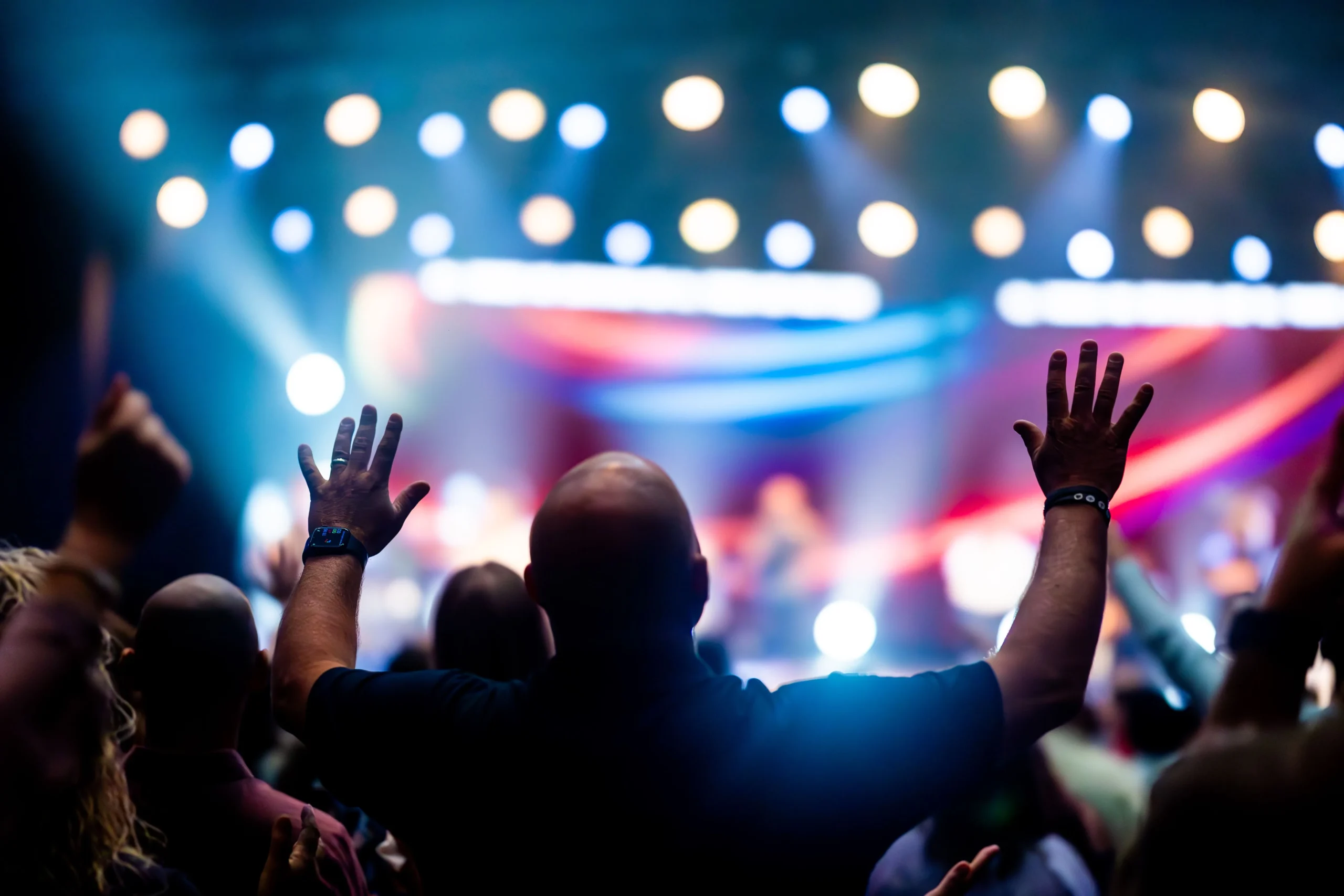 Concert stage from the crowd's point of view with a man raise both his hands up